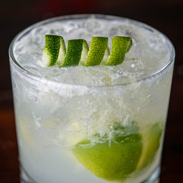 Close-up of a refreshing Cuban cocktail with ice, lime wedges, and lime peel garnish.