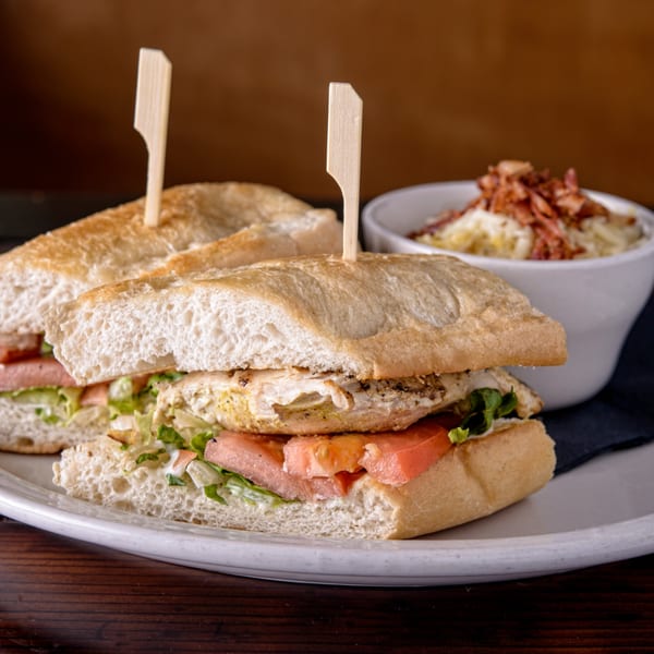 A Cuban chicken sandwich with lettuce and tomato, served with a side of mac and cheese.