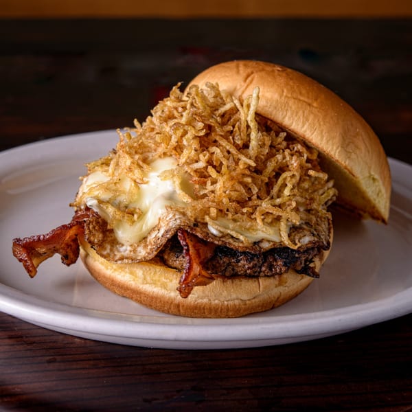A Cuban Burger with a fried egg, bacon, melted cheese, and crispy shoestring fries on a bun.