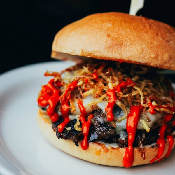 A Cuban Burger with melted cheese, crispy fried onions, and red sauce on a white plate.
