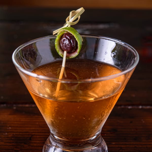 Close-up of a Cuban cocktail in a martini glass, garnished with a lime peel and olive.