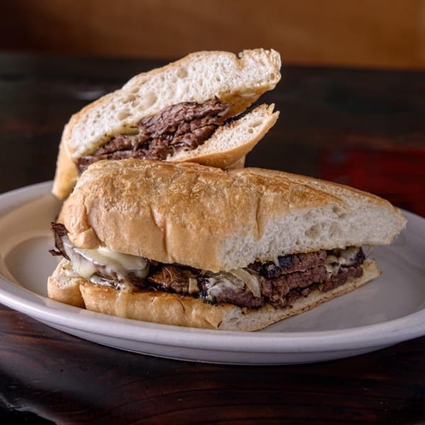 Two halves of a Cuban steak sandwich with melted cheese and onions on a white plate.