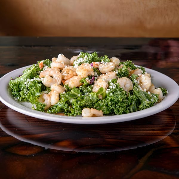 A vibrant Cuban shrimp salad with kale and crumbled cheese on a white plate.