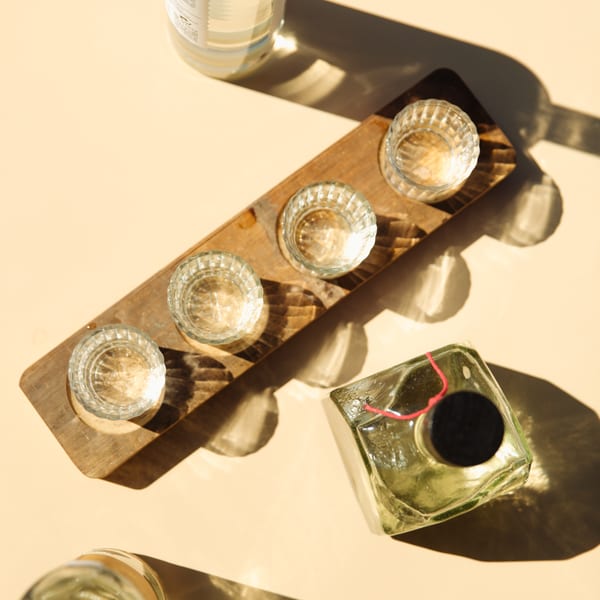 Overhead view of four empty shot glasses on a wooden tray with bottles on a sunny table.