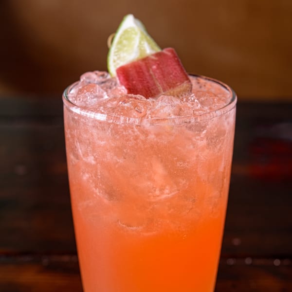 Close-up of a vibrant pink Cuban cocktail with ice, garnished with a lime wedge and a red fruit.