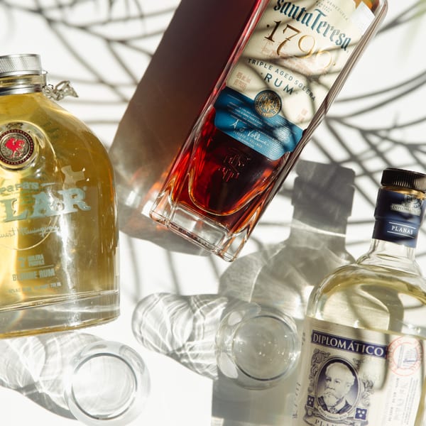 Three bottles of Cuban rum, Santa Teresa, Papa's Pilar, and Diplomatico, on a white surface.