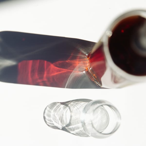 Overhead view of a glass of red wine and an empty glass, casting shadows and light patterns.