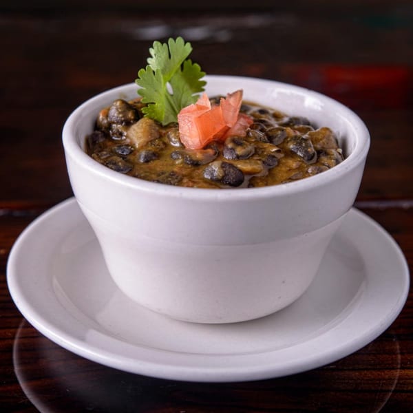 Cuban black beans and rice in a white bowl, garnished with cilantro and diced tomatoes.